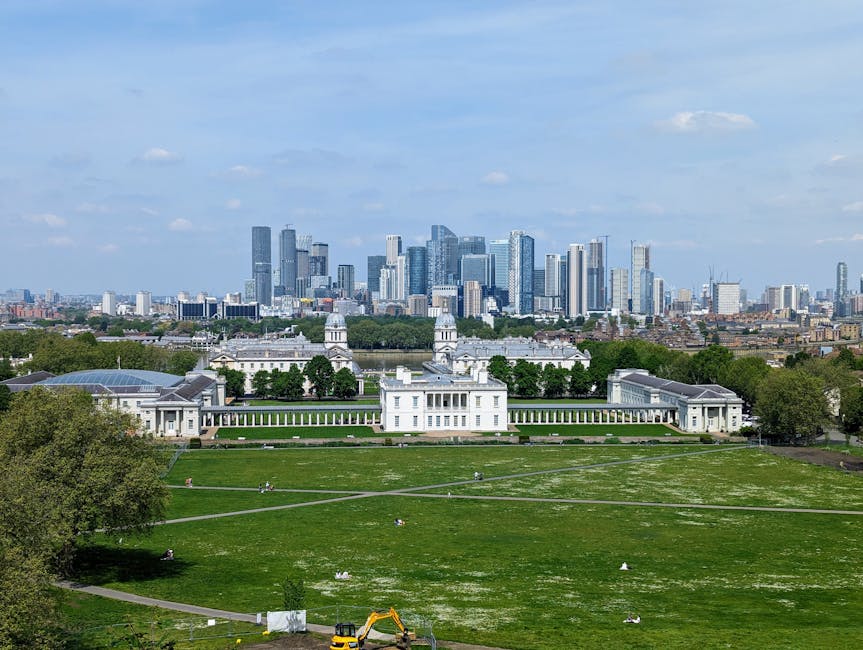 A view of a historic church with a domed tower featuring a golden weather vane, situated in the foreground of a modern city skyline with tall office buildings made of glass and steel. The church's arc